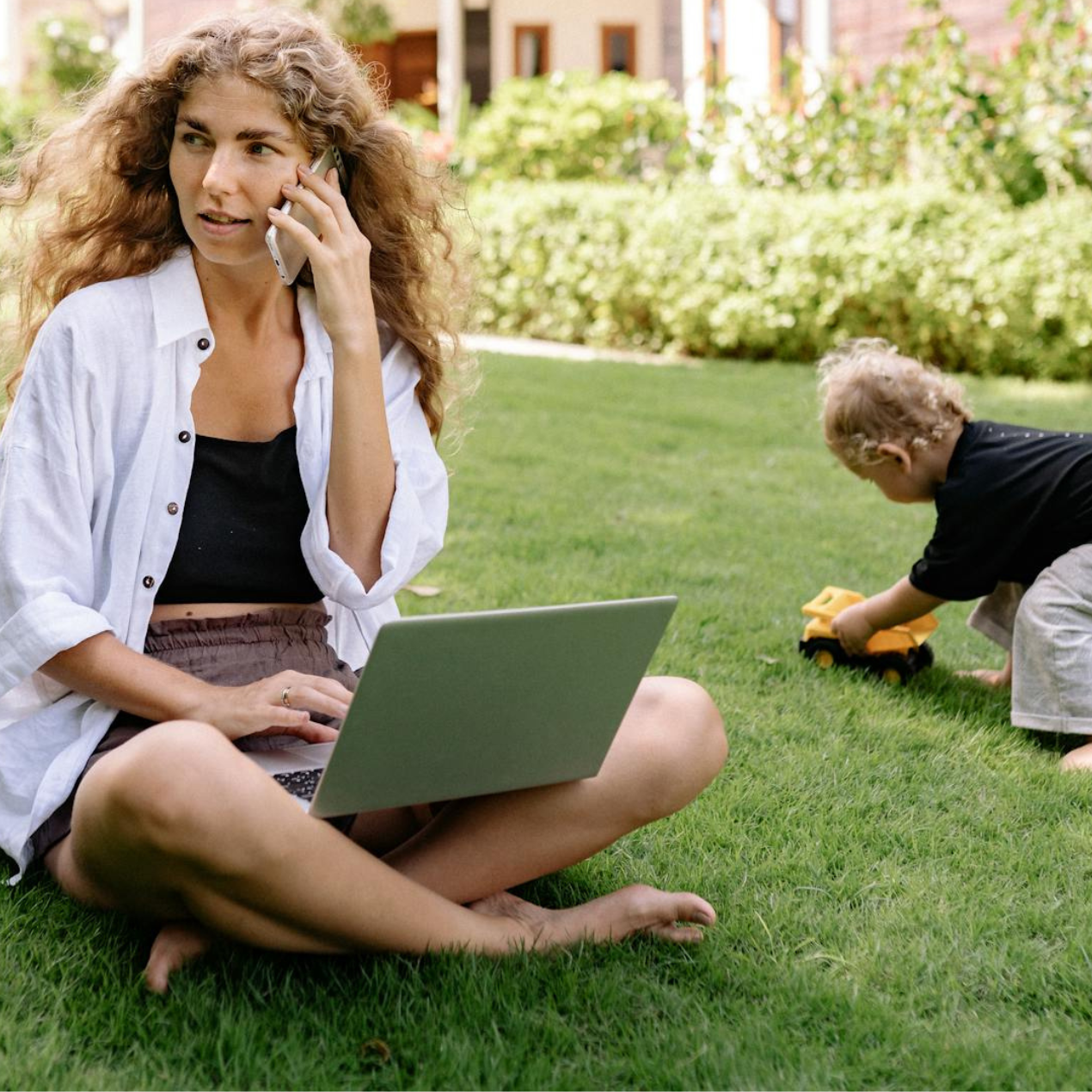 1 lady on the phone with laptop and child playing on the grass